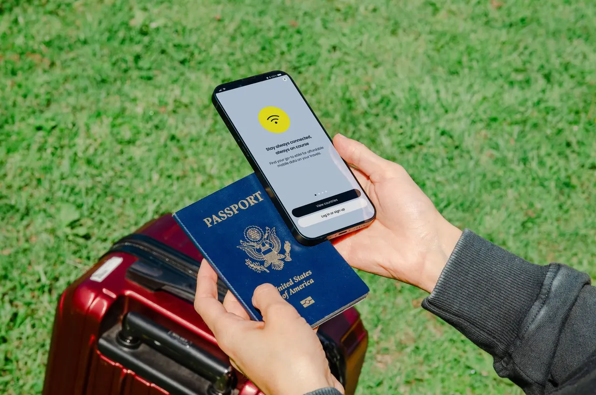 スーツケースの上でパスポートとスマートフォンを手に持つ旅行者の手元